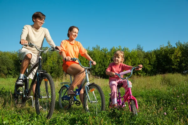 Отец, мама и дочь едут кататься на велосипеде в солнечный день — стоковое фото