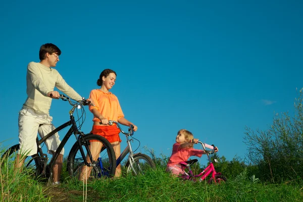 Сім'я з трьох осіб на велосипедах. Батьки дивляться на доньку — стокове фото