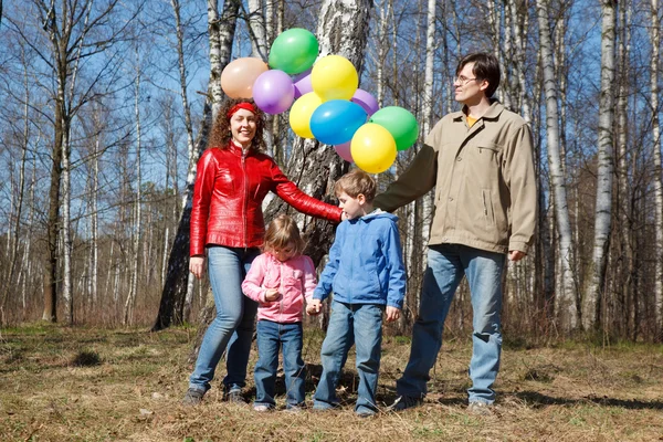 Родители с дочерью и сыном гуляют в парке с воздушными шарами — стоковое фото