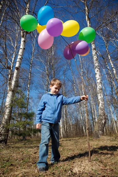 Мальчик с снопом воздушных шаров в парке весной — стоковое фото