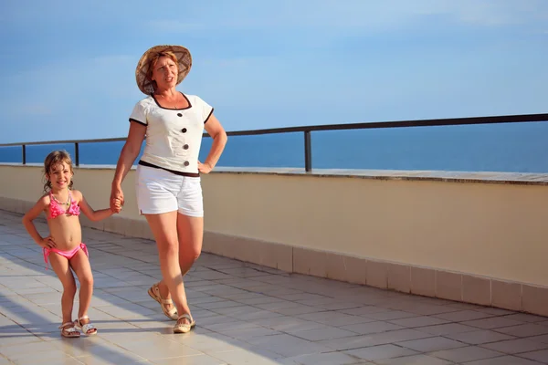 Starší žena a holčička chodí na verandě poblíž mořského pobřeží — Stock fotografie