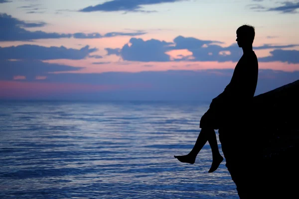 Silhouette guy sitting on breakwater in evening near sea — Stock Photo, Image