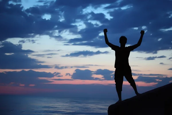 Silhouette guy lifted hands upwards on breakwater in evening nea — Stock Photo, Image