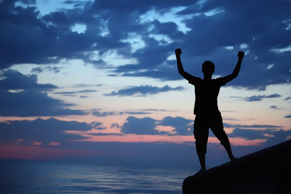 Silhouette guy lifted hands upwards on breakwater in evening nea