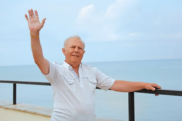 Lächelnder Senior auf der Veranda am Meer, erhobene Hand nach oben — Stockfoto