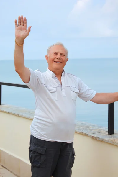 Lächelnder Senior auf der Veranda am Ufer des Meeres, erhob die Hand nach oben, — Stockfoto