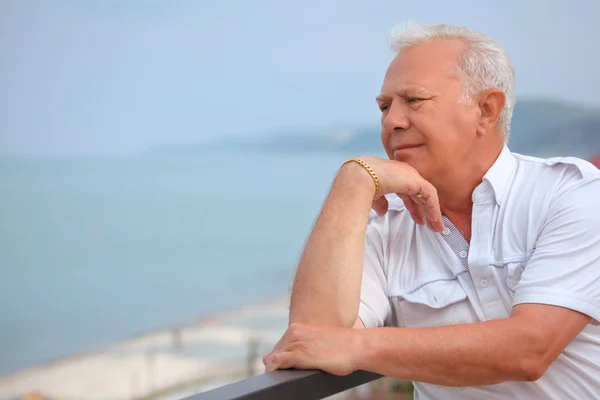 Smutný senior na verandě nedaleko mořského pobřeží, hledá dálky, opřít lokty — Stock fotografie