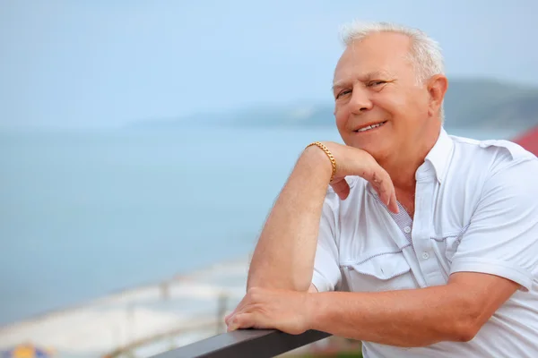 Lächelnder Senior auf der Veranda am Ufer des Meeres, Ellbogen um die Hand gebeugt — Stockfoto