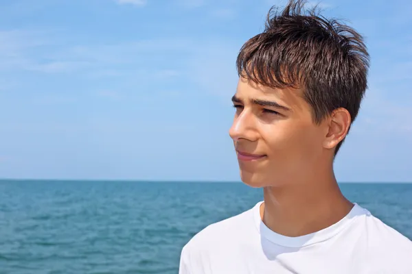 Улыбающийся мальчик-подросток на фоне моря, глядя издалека — стоковое фото