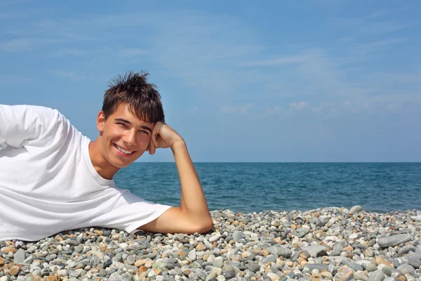 Adolescente menino em branco t-shirt deitado no pedregoso seacoast — Fotografia de Stock