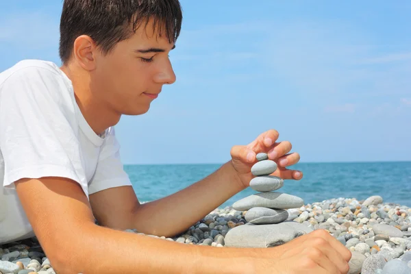 Adolescente niño acostado en la costa pedregosa, crea pirámide de pebbl —  Fotos de Stock