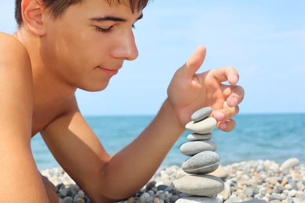 Genç çocuk taşlı sahil üzerinde yalan pebbl piramit oluşturur — Stok fotoğraf