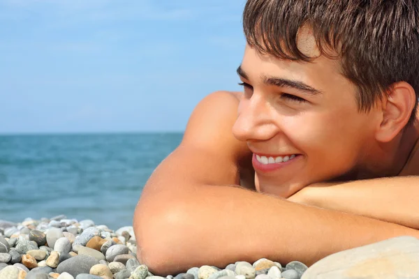 Tiener jongen liggend op steenachtige Zeekust, op zoek naar de verte — Stockfoto