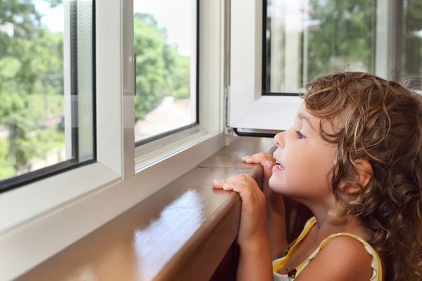 漂亮微笑着阳台上的小女孩，从窗口看 — 图库照片