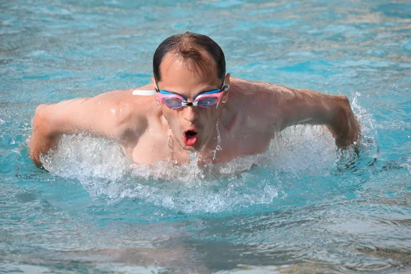 Hombre joven en gafas de deporte acuático nadando en la piscina, saltó fuera de —  Fotos de Stock
