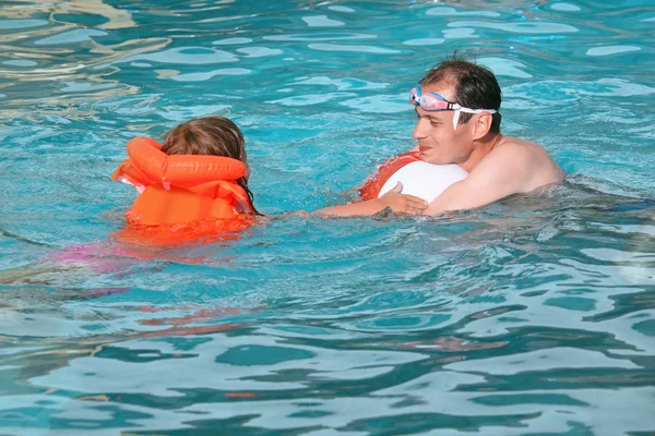 Young man and little girl in lifejacket bathing in pool on reso — Stock Photo, Image
