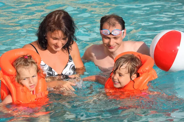 Dos niñas pequeñas bañándose en chalecos salvavidas con los padres en la piscina en —  Fotos de Stock