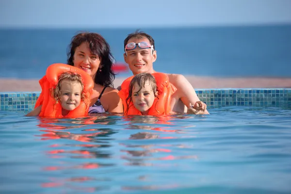 Дві маленькі дівчата купаються в рятувальних жилах з батьками в басейні — стокове фото