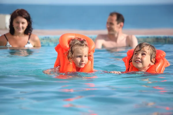 Две маленькие девочки купаются в спасательных жилетах с родителями в бассейне на — стоковое фото