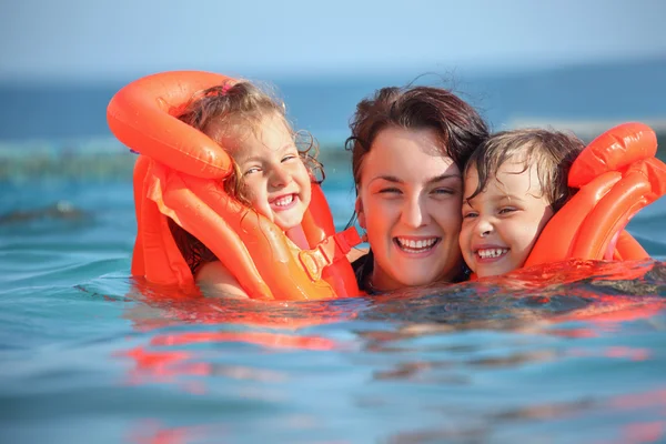 Две маленькие девочки купаются в спасательных жилетах с молодой женщиной в бассейне — стоковое фото