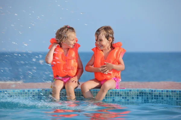 Two little girls in lifejackets sitting on ledge pool on resort, — Stock Photo, Image