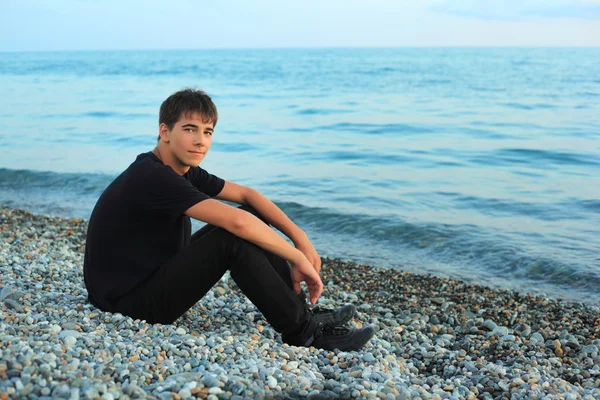 Sentado adolescente menino em pedra litoral perto do mar — Fotografia de Stock