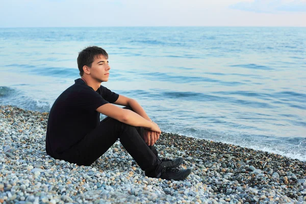 Ülő tizenéves fiú kő seacoast látszó messze — Stock Fotó