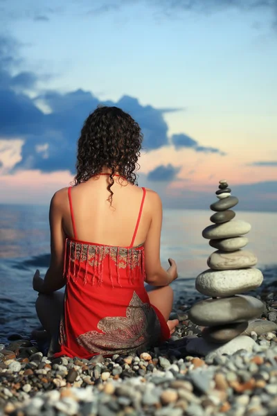 Beautiful woman in red sundress meditating near to pyramid from — Stock Photo, Image