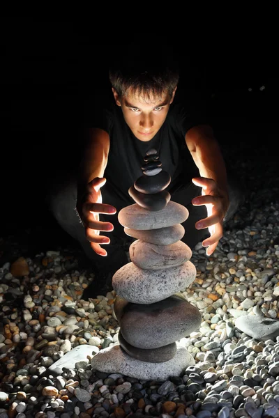 Adolescente menino conjurando perto pirâmide de seixo em seacoas pedregosas — Fotografia de Stock