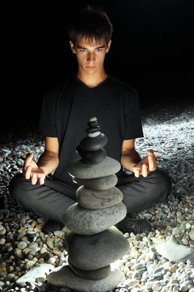 Menino adolescente meditando perto da pirâmide de seixo no mar pedregoso — Fotografia de Stock