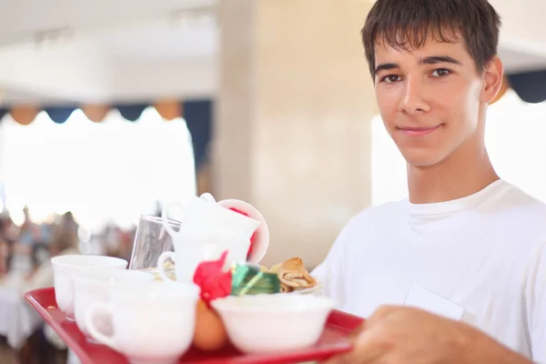 stock image Young smiling affable waiter keeps tray with dishes at restauran