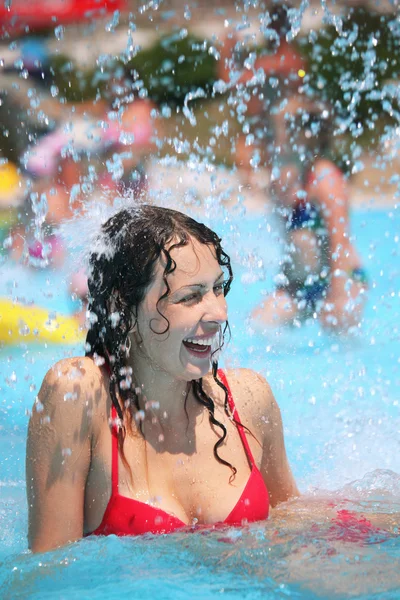 Souriant belle femme se baigne dans la piscine sous les éclaboussures d'eau — Photo