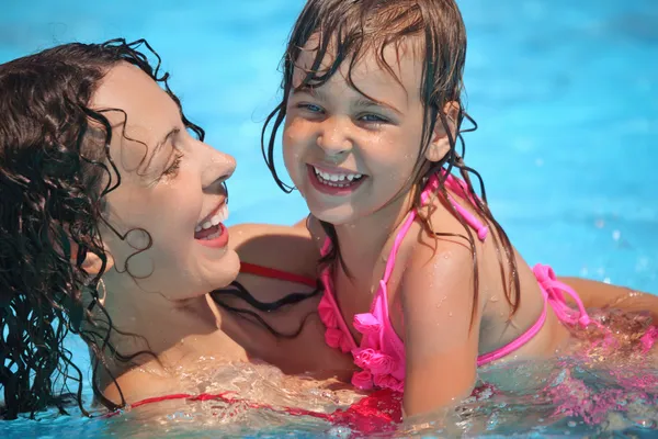 Sonriente hermosa mujer y niña se baña en la piscina — Foto de Stock