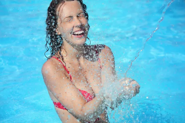 Mooie vrouw glimlachend baadt in zwembad onder water spatten, clo — Stockfoto