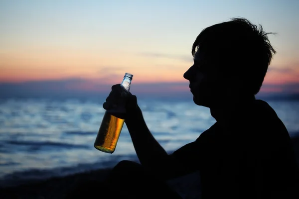 Silhouette teenager boy with beer bottler on stone seacoast in e — Stock Photo, Image