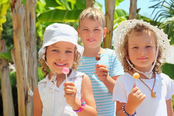 Gülümseyen çocuklar üç birlikte parkta lolipop yemek — Stok fotoğraf