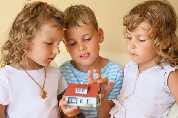 Dzieci trzy razem trzymając w ręce model domu w przytulny — Zdjęcie stockowe