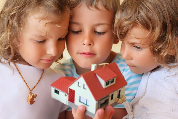 Crianças três em conjunto que guardam em mãos o modelo da casa no acolhedor — Fotografia de Stock