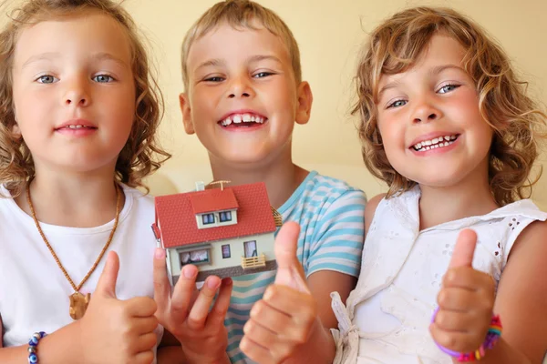 Kinder drei zusammen halten Modell des Hauses in gemütlicher Atmosphäre in Händen — Stockfoto