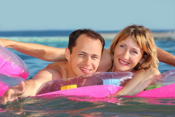 Jonge man en mooie vrouwen, liggend op een opblaasbare matras in zwembad — Stockfoto