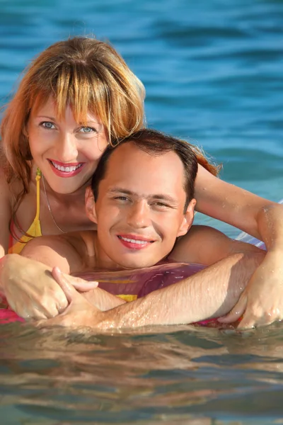 Hombre joven y mujeres agradables que mienten en un colchón inflable en la piscina —  Fotos de Stock
