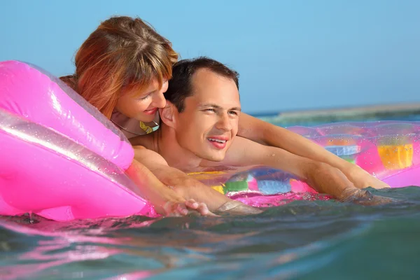 Mladý muž a hezké ženy na nafukovací matraci v bazénu — Stock fotografie