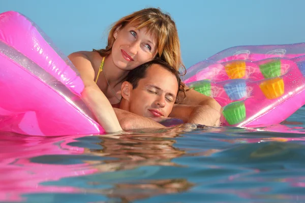 Hombre joven y mujeres agradables que mienten en un colchón inflable en la piscina —  Fotos de Stock