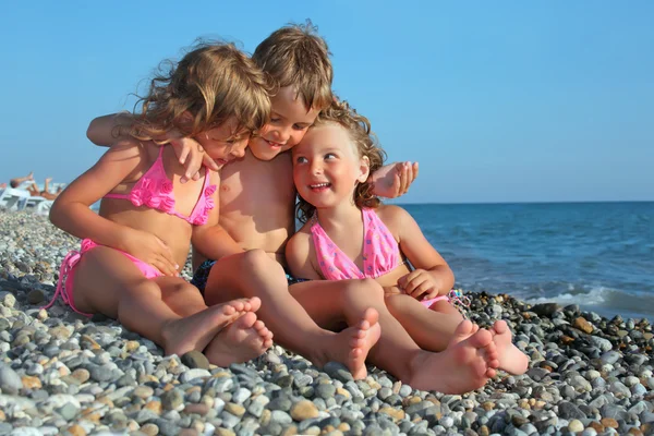 Παιδιά τριών μαζί κάθεται στην πετρώδη παραλία — Φωτογραφία Αρχείου