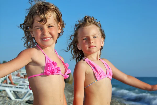 Two pretty little girls on beach near sea, placed hands in sides — Stock Photo, Image