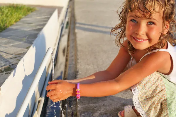 Smiling little girl washes hands water from pipe in street — Stock Photo, Image