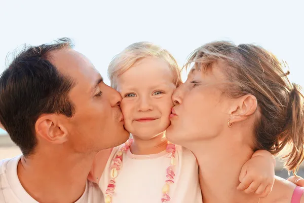 Щаслива сім'я з мало близькою до моря, батьки цілують дочку — стокове фото