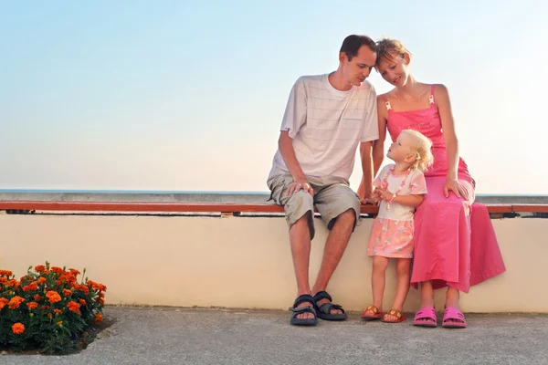 Счастливая семья с маленьким сидящим на скамейке на курорте — стоковое фото