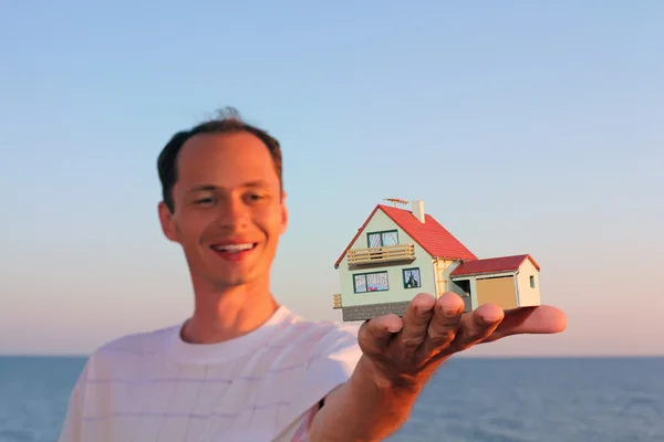 Joven hombre mantiene en la mano modelo de casa con garaje —  Fotos de Stock