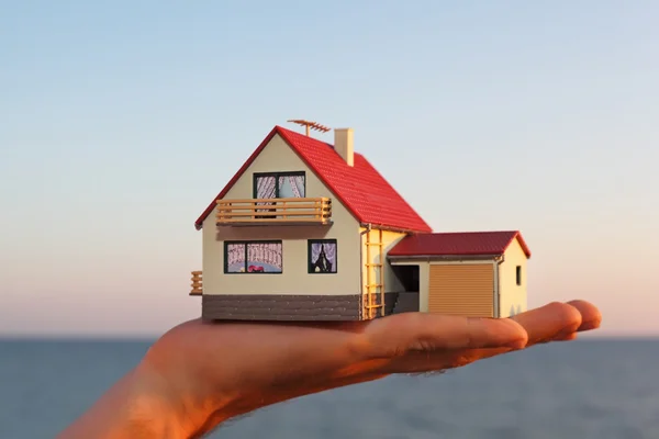 Modell eines Hauses mit Garage an der Hand gegen Meer — Stockfoto